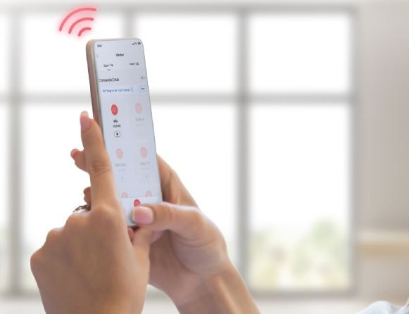 Dámské ruce drží mobilní telefon a prostřednictvím aplikace sledují průběh pračky na dálku.