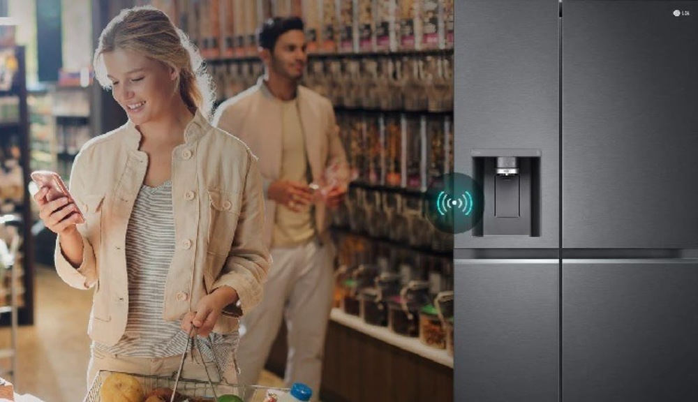 Americká lednice LG GSLE81PYBC nerez žena v obchodě kontroluje stav americké lednice LG pomocí mobilni aplikace LG, za ni stojí muž.