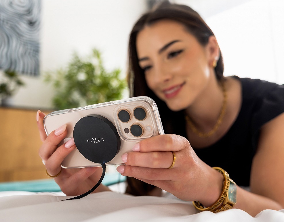 Žena drží v rukou růžový telefon uchycený na bezdrátovou nabíječku FIXED MagPad Slim s Qi2, MagSafe