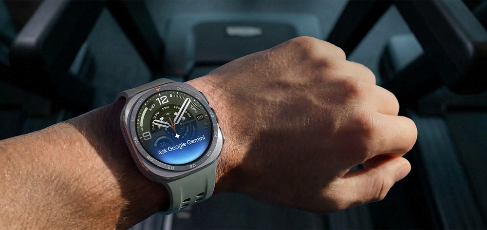 Člověk na běžícím pásu má na ruce hodinky Galaxy Watch Ultra2 v barevném provedení Titanium Silver se sportovním řemínkem Marine Band v barvě Olive a zvednutým zápěstím, na kterém se zobrazuje text „Ask Google Gemini“ (Zeptat se Google Gemini), zvýrazňujíc funkci Raise-to-Talk (Zvedni a mluv) na Galaxy Watch Ultra2.