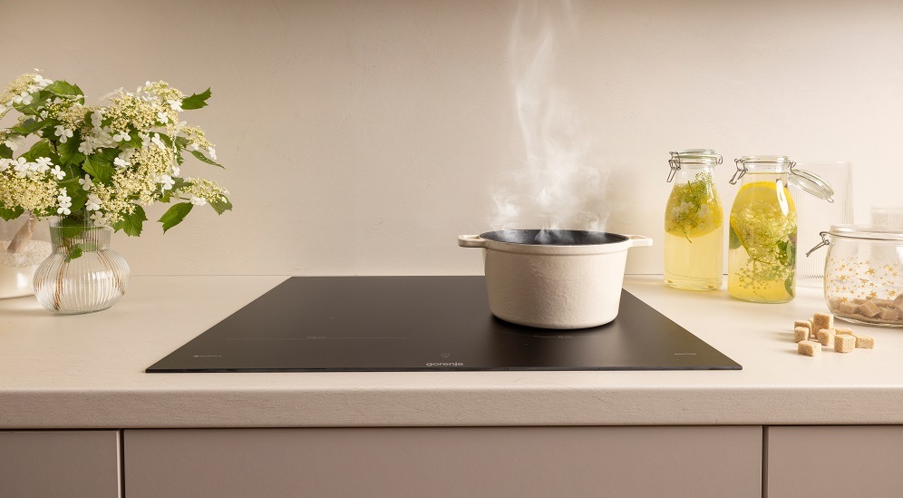 Indukční varná deska Gorenje G600 GI6442MSCWF InfiniteMatt černá Kouřící hrnec stojí na varné desce gorenje ve světlé kuchyni. Vedle desky je vaza s květinami a na druhe straně skleněné nádoby s limonadou.