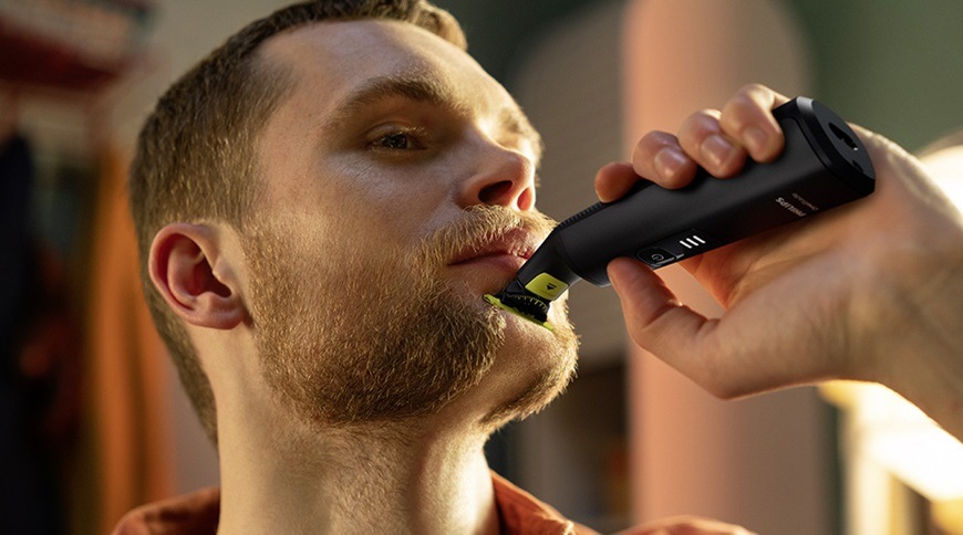 Náhradní hlavice Philips OneBlade QP945/50 stříbrná Muž používá holicí strojek Philips OneBlade s náhradní hlavicí QP945/50 při úpravě vousů na bradě, přístroj je přiložený k pokožce obličeje.