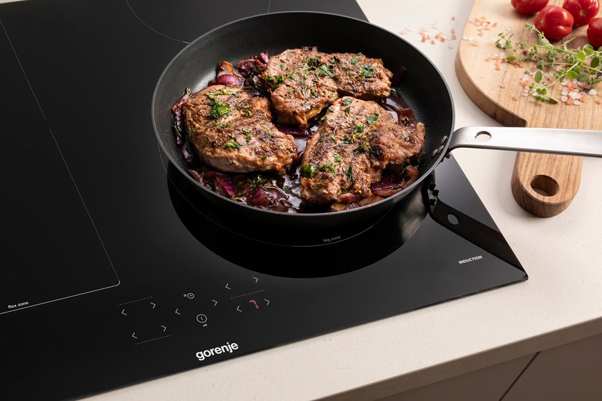 Na indukční varné desce Gorenje GI6431BFG se na pánvi připravuje maso v moderní kuchyni.