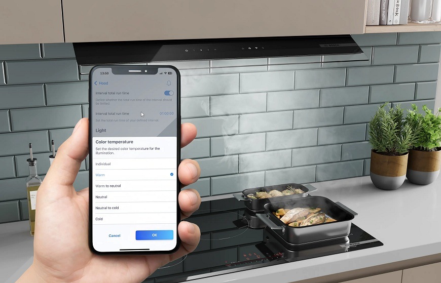 Náhled na mobilní telefon s aplikaci Home Connect, v pozadí varná deska a odsavač par