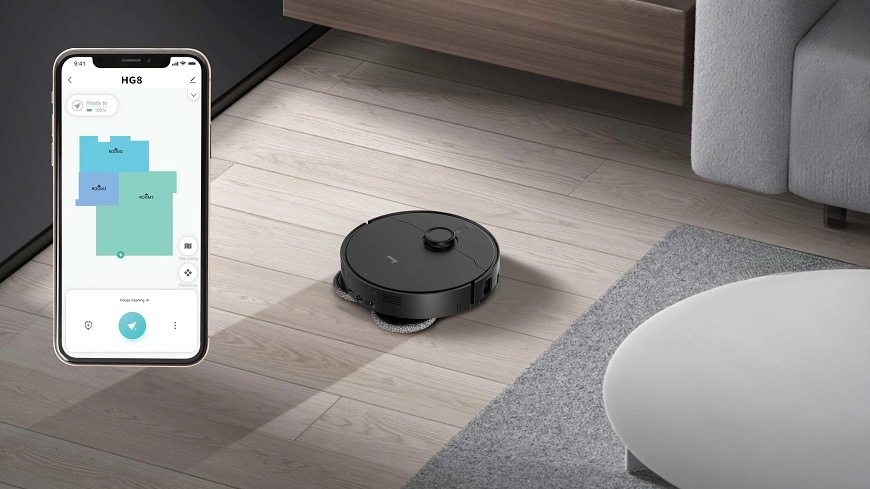 Robotický vysavač Hoover HG870HU 011 zanechává na podlaze za sebou vlhkou cestu, na telefonu je vidět mapa místností v aplikaci