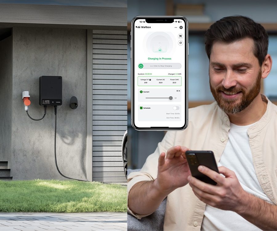 Wallbox dé namontovaný u garáže, muž vedle něj ovládá nabíjení přes telefon.