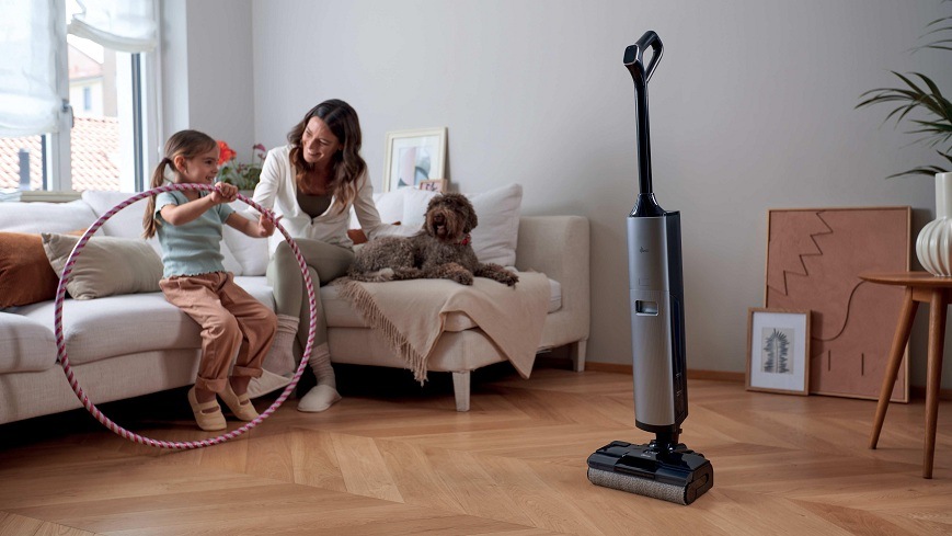 Podlahová myčka Hoover HW600 011 černý/světle šedý vysavač Hoover HW600 011 stojí uprostřed místnosti, zatímco žena s dcerou a psem sedí spolu na gauči