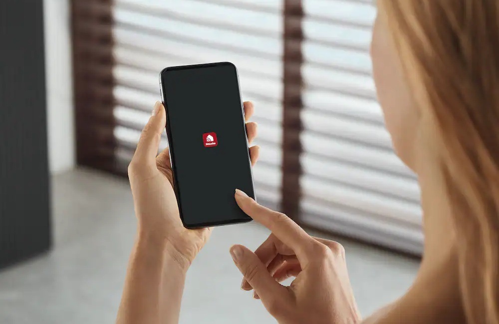 Indukční varná deska s odsáváním Miele KMDA 7676-1 FL černá Žena drží v ruce mobilní telefon, na displeji je aplikace Miele