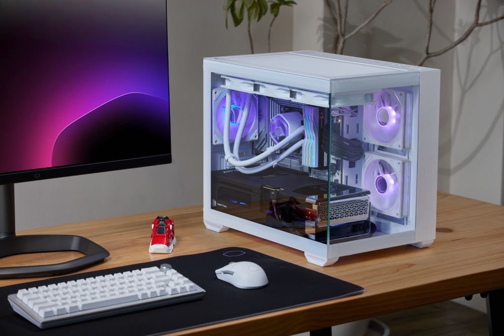 Case Cooler Master Elite 481 Wood ARGB bílá Elegantní bílá počítačová skříň se svítícími fialovými ventilátory na dřevěném stole, vedle monitoru zobrazujícího fialové odstíny, klávesnice, myši a malou botou.