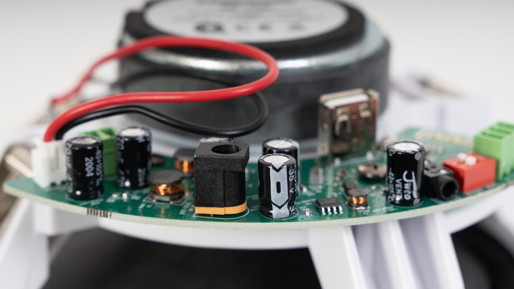 Detail elektroniky aktivního reproduktoru s obvodovou deskou, konektory, součástkami a magnetem.