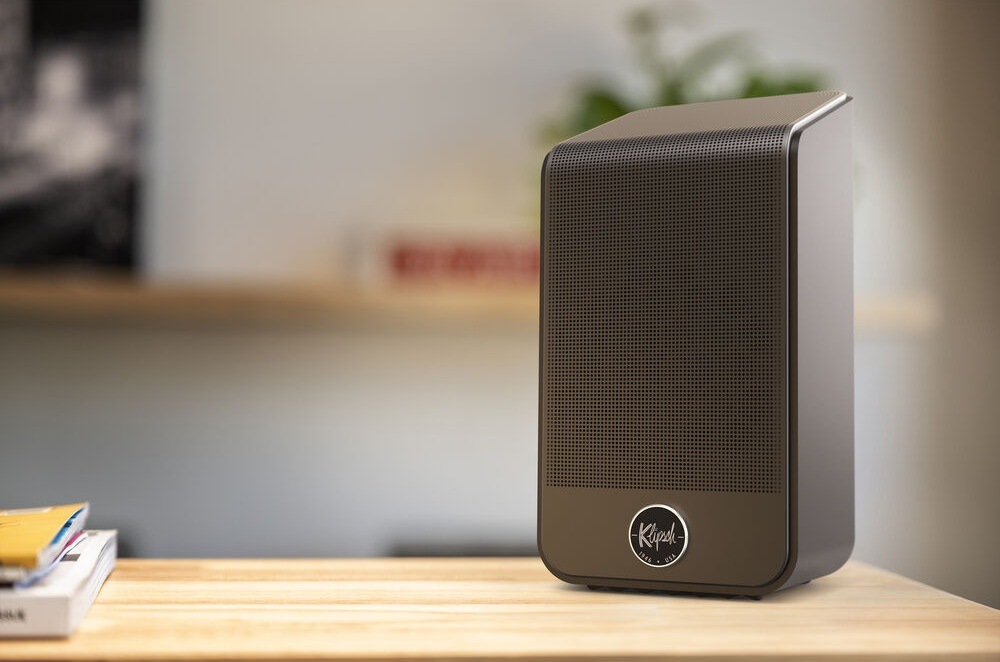 Reproduktory Klipsch Flexus SURR 200 (2 ks) černé Jeden reproduktor Klipsch Flexus SURR 200 stojí na stole, vlevo na stole leží sešity, na pozadí je rozostřená místnost
