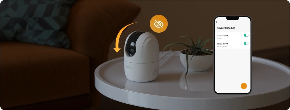IP kamera Imou Ranger 2C Pro bílá IP kamera Imou stojí na stolku vedle rostliny. Oranžová šipka a ikona přeškrtnutého oka ukazují režim soukromí, kdy se objektiv kamery sklopí. Vpravo je mobilní aplikace s plánem soukromí pro automatické vypnutí sledování.