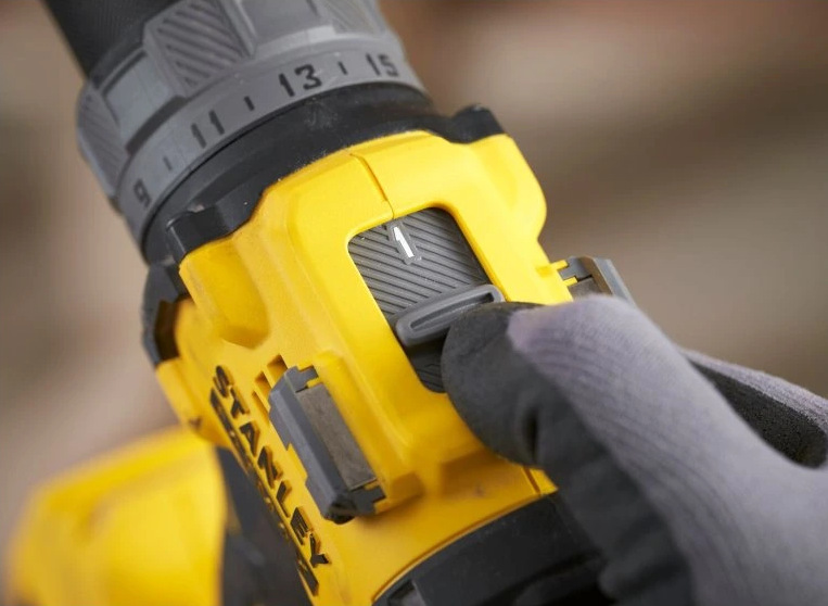 Detail přepínače rychlostí aku vrtačky Stanley FatMax V20 v rukavicí chráněné ruce.
