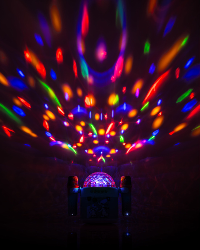 Dětský růžový karaoke reproduktor GoGEN Bob a Bobek s disko koulí, která promítá barevná světla (červená, modrá, zelená) na strop a stěny tmavé místnosti. Po stranách jsou připojené dva mikrofony