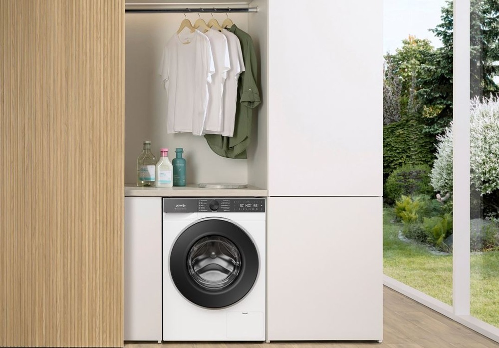 Pračka Gorenje G600 WG614A4P1 FastWashPro bílá pračka Gorenje WG614A4P1 FastWashPro zabudovana v dřevěné skřínove stěně. Nad ní visi na raminku trička. Vedle jsou prosklené dveře do zahrady