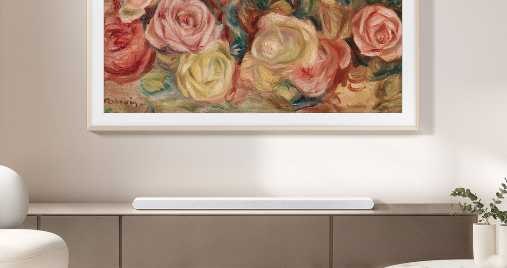 Soundbar Samsung HW-S701D bílý Bílý soundbar Samsung HW-S701D leží na skříňce v obývacím pokoji pod televizí Samsung Frame pověšené na zdi