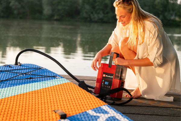Kompresor Einhell SUPPERO 18/380 Li při nafukování paddleboardu na pláži.