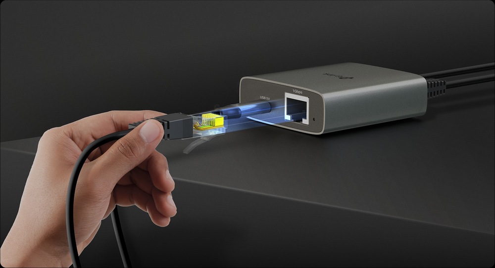 Ruka drží zářící síťový kabel a zapojuje jej do elegantního kovového zařízení na tmavém povrchu. Scéna vyzařuje moderní technologický nádech.