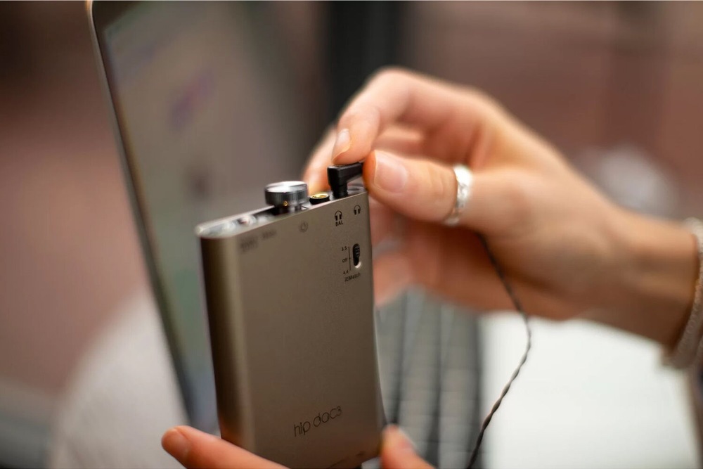 Připojování sluchátek k zesilovači iFi hip-dac 3 vedle notebooku.