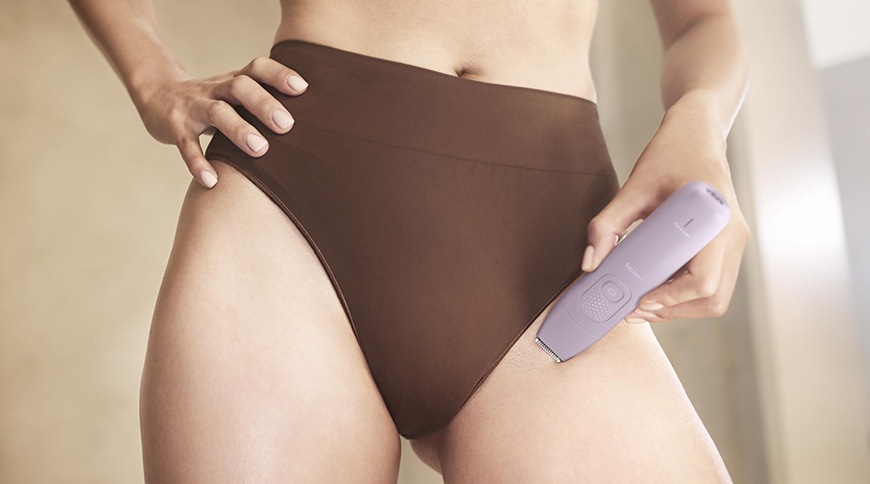 Detail použití epilátoru Philips BRE728/00 ve fialové barvě v oblasti třísel, přístroj je přiložený k pokožce stehna během odstraňování chloupků.