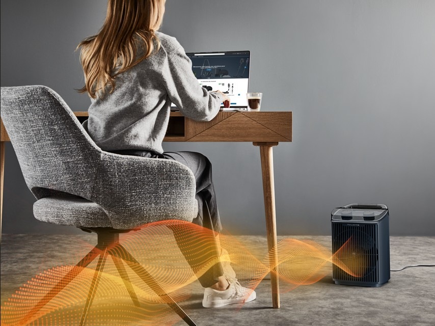 Teplovzdušný ventilátor Rowenta SO6551F0 Intense Comfort Aqua černý Žena sedí i stolu a pracuje na počítači a vedle ní teplovzdušný ventilátor Rowenta SO6551F0 Intense Comfort Aqua