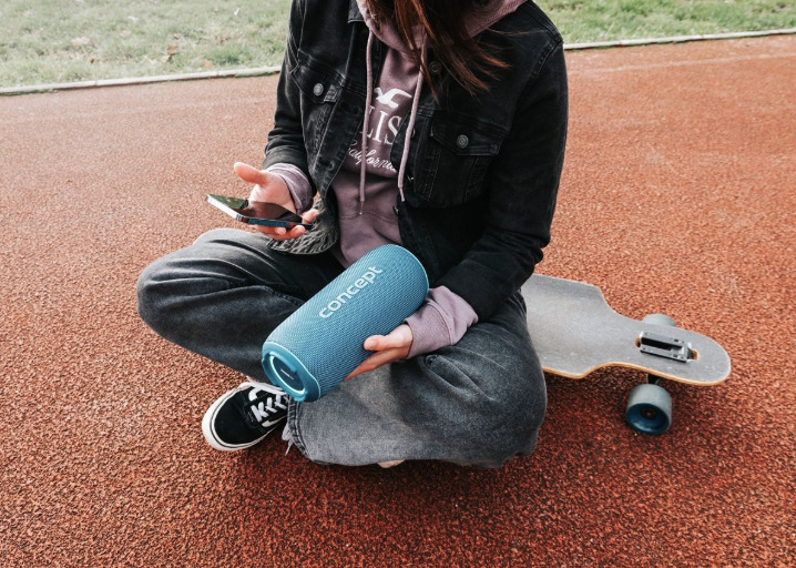 Žena sedí vedle skateboardu a drží reproduktor Concept SoundJoy BR5532 propojený s telefonem