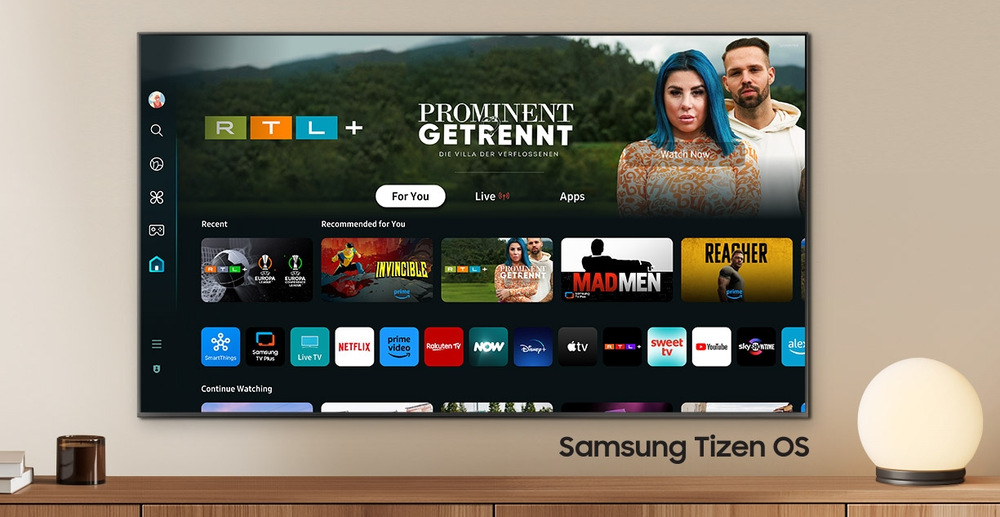 Televize Samsung QE55S85DA Televize pověšená na zdi místnosti, na obrazovce je domovská stránka OS Tizen s nabídkou aplikací a obsahu