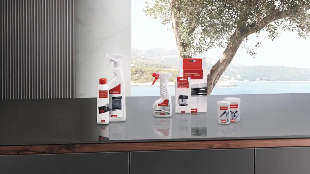 Čisticí přípravek Miele 500 ml OvenClean GP CL H 0502 L položený na kuchyňské lince s dalšími čisticími přípravky