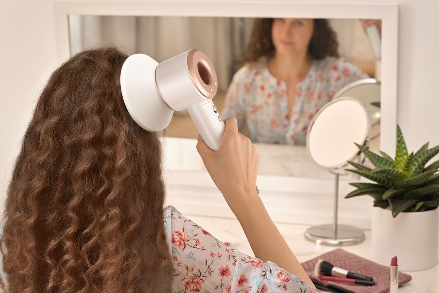 Žena si fénuje vlasy fénem Sencor SHD 8900RS s difuzérem před zrcadlem v koupelně, styling vlnitých vlasů.