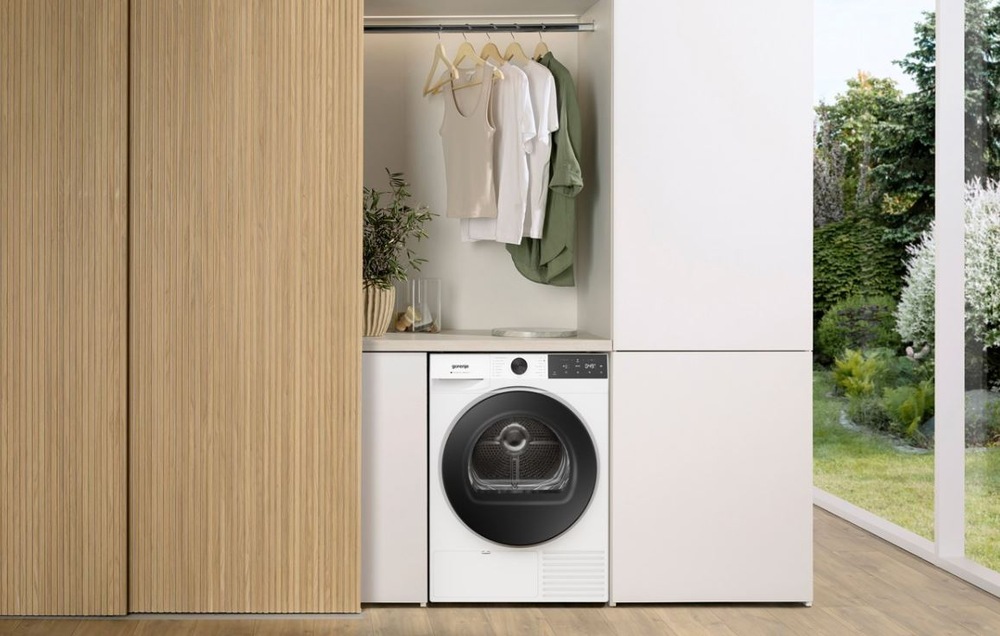 Sušička prádla Gorenje G400 DG48D NatureDry černá sušička Gorenje DG48C NatureDry umístěná vedle šatní skříně v dřevěném dekoru, na druhe straně je prosklenny vstup na zahradu. Nad sušičkou visi na raminku trička.