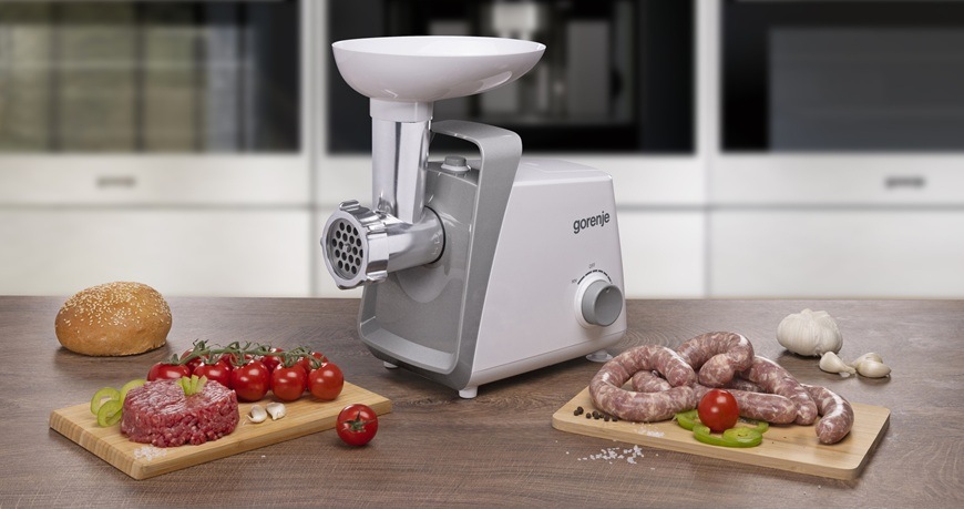 Mlýnek na maso Gorenje MG1601W bílý Mlýnek na maso Gorenje MG1601W je položený na stole a kolem něj jsou rozmístěné různé druhy pokrmů.