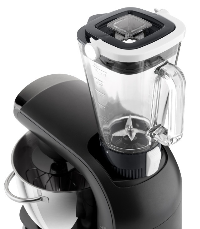 Skleněný mixovací nástavec kuchyňského robota ETA Gratus Evo Origin II naplněný čerstvým ovocem (jahody, kiwi, banán, mango). Pohled shora demonstruje horní vývod pro mixování smoothies a koktejlů, zatímco v nerezové míse je nasazena šlehací metla pro souběžnou přípravu