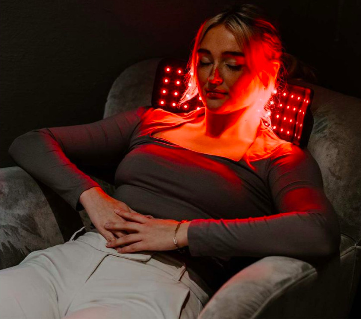 Žena používá návlek pro LED terapii v oblasti šíje při odpočinku v křesle