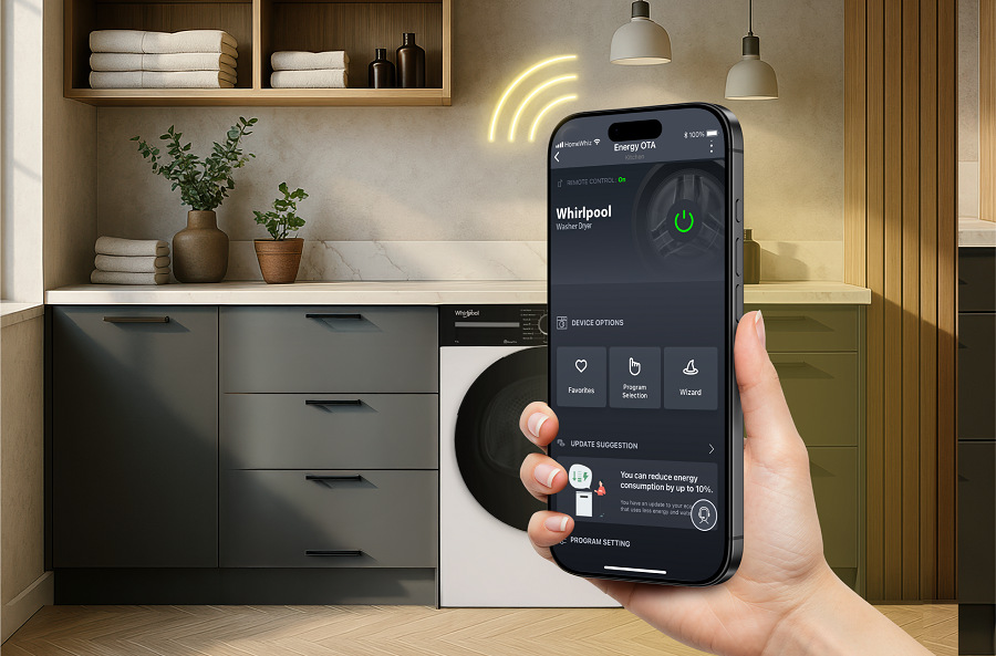 RRuka držící chytrý telefon s aplikací HomeWhiz v pozadí pračka Whirlpool v prádelně s poskládaným prádlem na skříňce