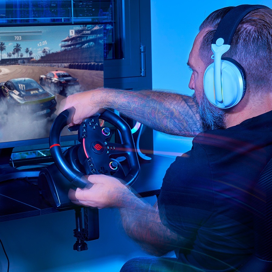 Volant SUPERDRIVE 270 GT-5 černý Muž se sluchátky a tetováním intenzivně hraje závodní videohru pomocí ovladače na volantu s modrým ambientním osvětlením.