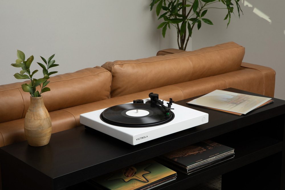 Bílý gramofon Victrola VPT-1520 Wave umístěný na stolku v obývacím pokoji, přehrává vinylovou desku v moderním interiér