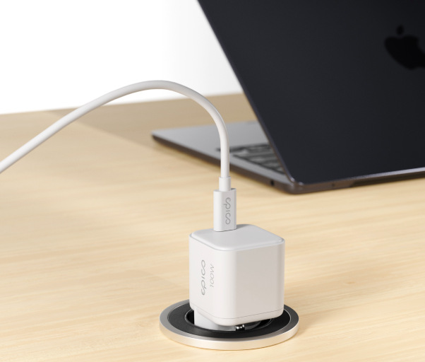 Napájecí adaptér Epico UltraBoost Micro AVS GaN 100W zapojený do zásuvky stolu při nabíjení notebooku