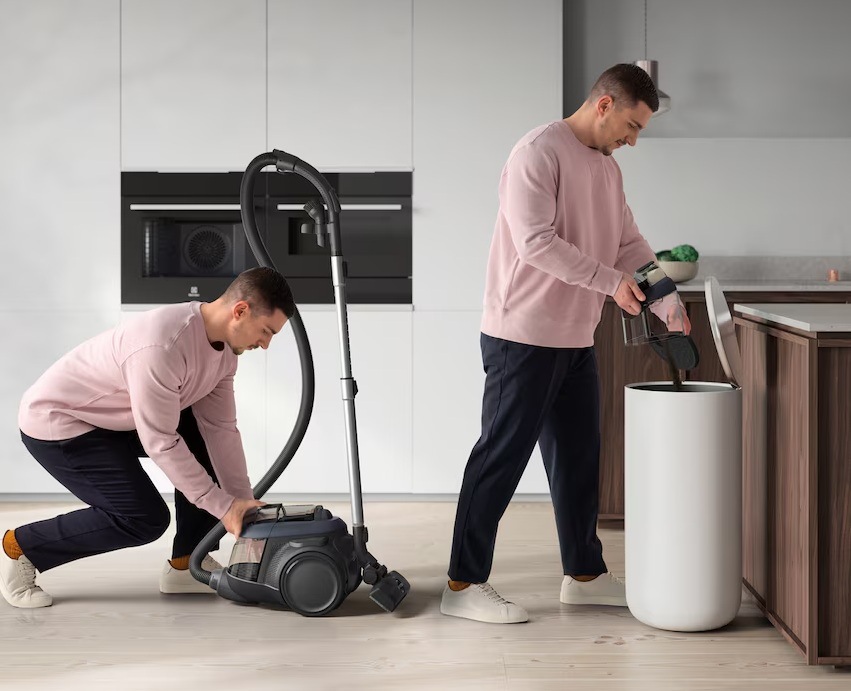 Muž vyndává prachovou nádobu z vysavače Electrolux a v dalším kroku vysypává její obsah do koše. V pozadí je kuchyně s vestavnými spotřebiči Electrolux.