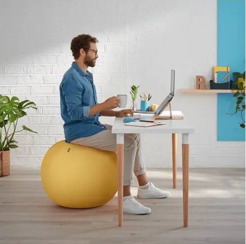 Muž používá sedací míč Leitz Ergo Cosy jako aktivní sezení při práci u stolu