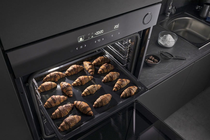 Na obrázku je otevřená trouba Hisense BSA66346PBGWIFI. Uvnitř ní se právě upekly mražené croissanty, vestavná, program pro mražená jídla