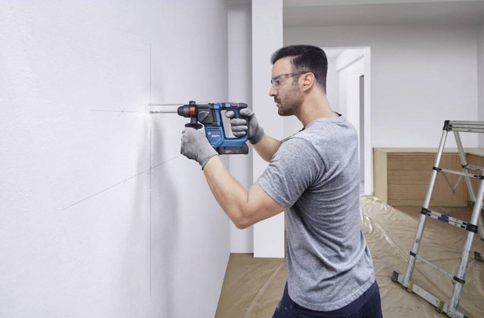 Muž při domácí rekonstrukci s lehkostí manipuluje s vrtacím kladivem Bosch Professional GBH 18V u stěny.