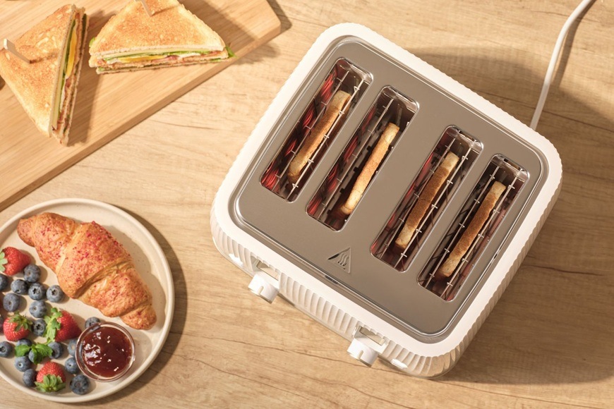 Topinkovač Sencor STS 7540WH bílý Pohled shora na topinkovač Sencor STS 7540WH se čtyřmi opékanými toasty na kuchyňské lince vedle croissantu, ovoce a sendviče.