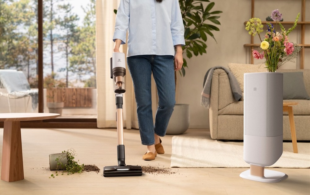 Tyčový vysavač Electrolux 800 Hygienic UV EP83HB25UV bílý Žena v obývacím pokoji vysává hlínu z převrhlého květináče