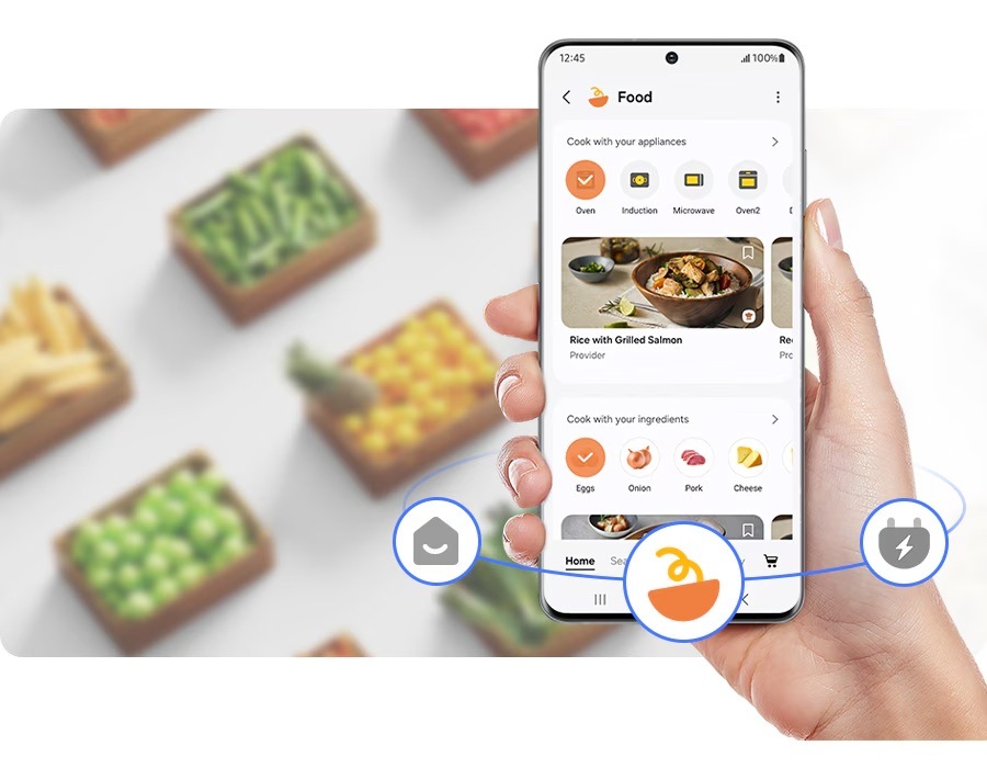 Ruka drží mobilní telefon s aplikací SmartThings Food, na pozadí jsou krabice s potravinami