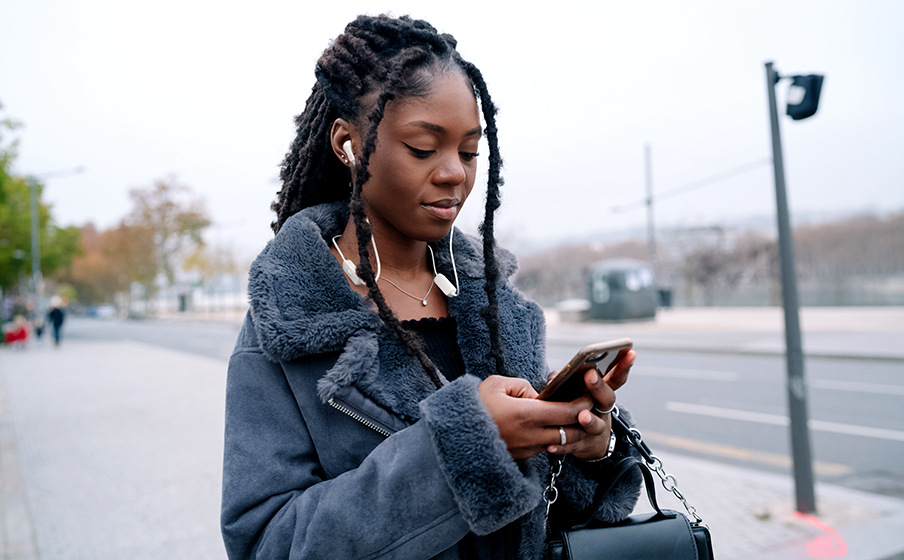 Žena dívající se do telefonu ma nasazená sluchátka JBL Tune 135BT