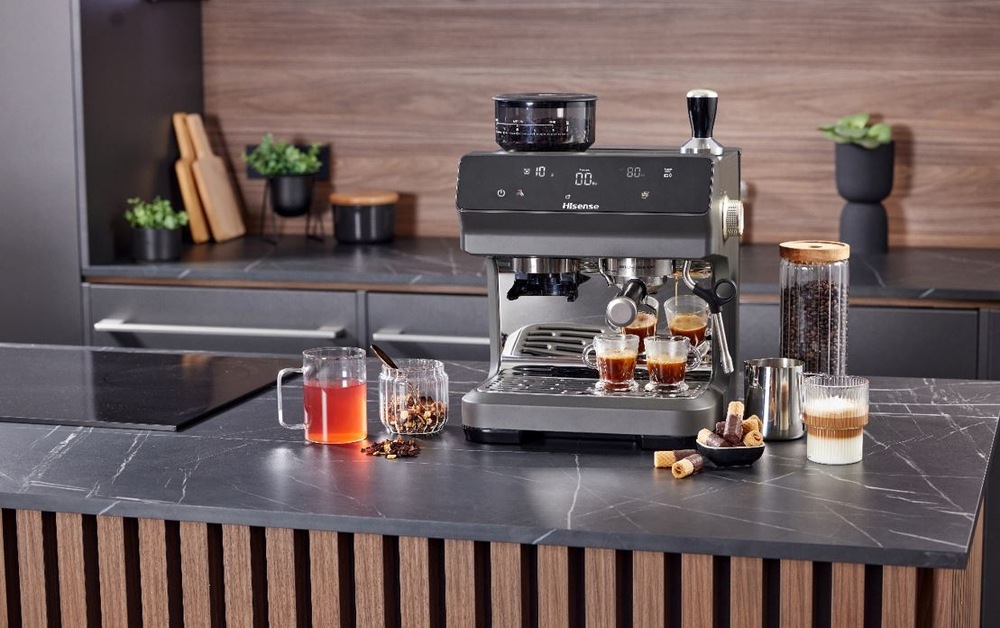 Espresso Hisense HSACM20LP antracitový pákový kávovar Hisense HSACM20LP na černé kuchynské desce. Připravuje dvě epressa a vedle stoji latte ve sklence. Na druhe straně je čaj.