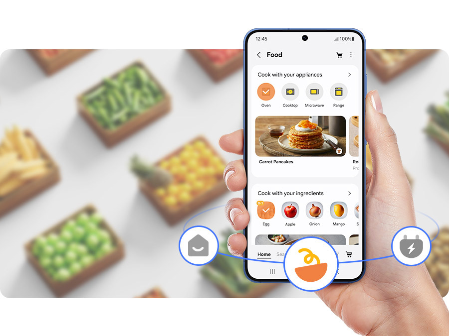 Americká lednice Samsung RM70F63NEREO nerez/ocel Ruka drží mobilní telefon s otevřenou aplikací SmartThings Food, na pozadí jsou krabice s jídlem
