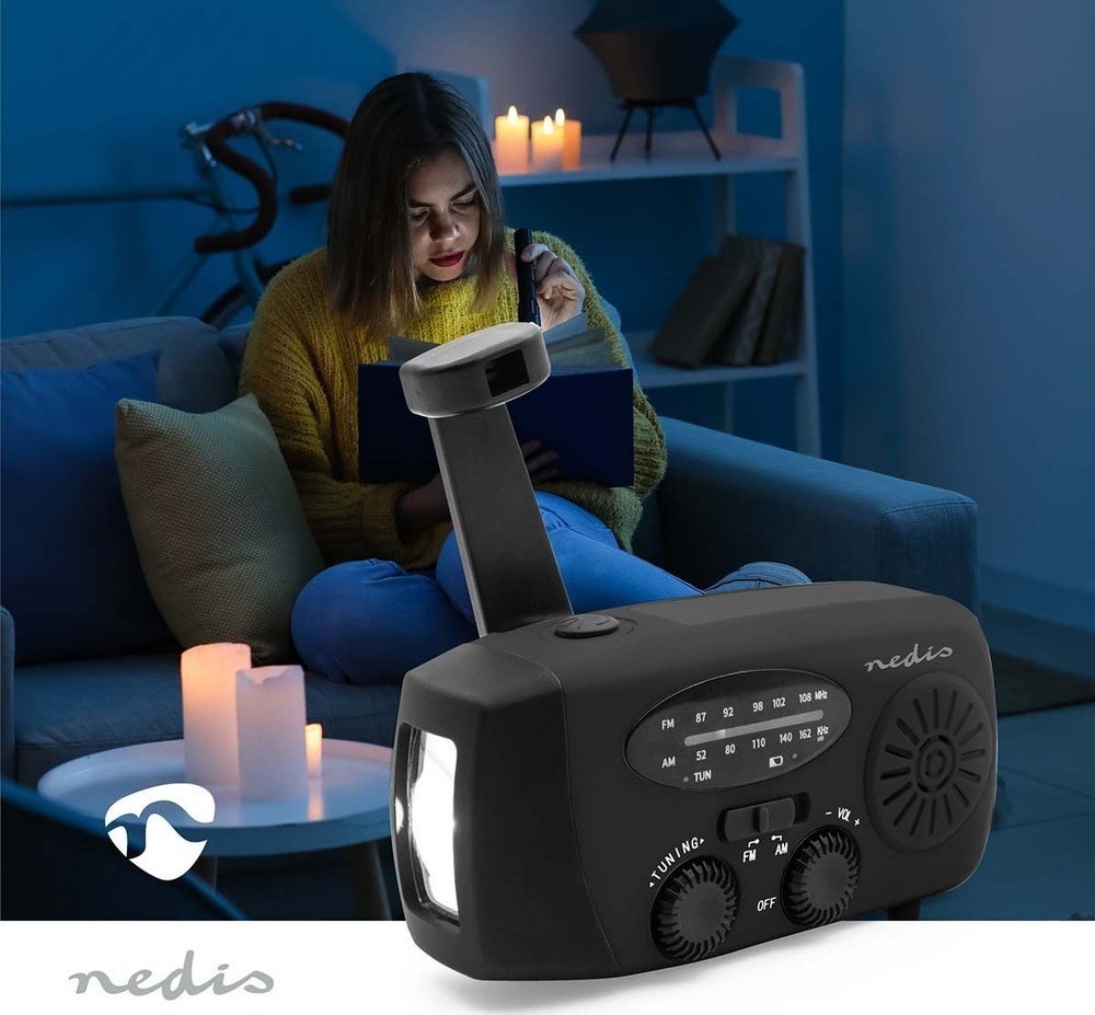 Radiopřijímač Nedis RDFMCR2000 černý Žena čte při výpadku proudu za svitu svíček, v popředí nouzové rádio Nedis se svítící baterkou.