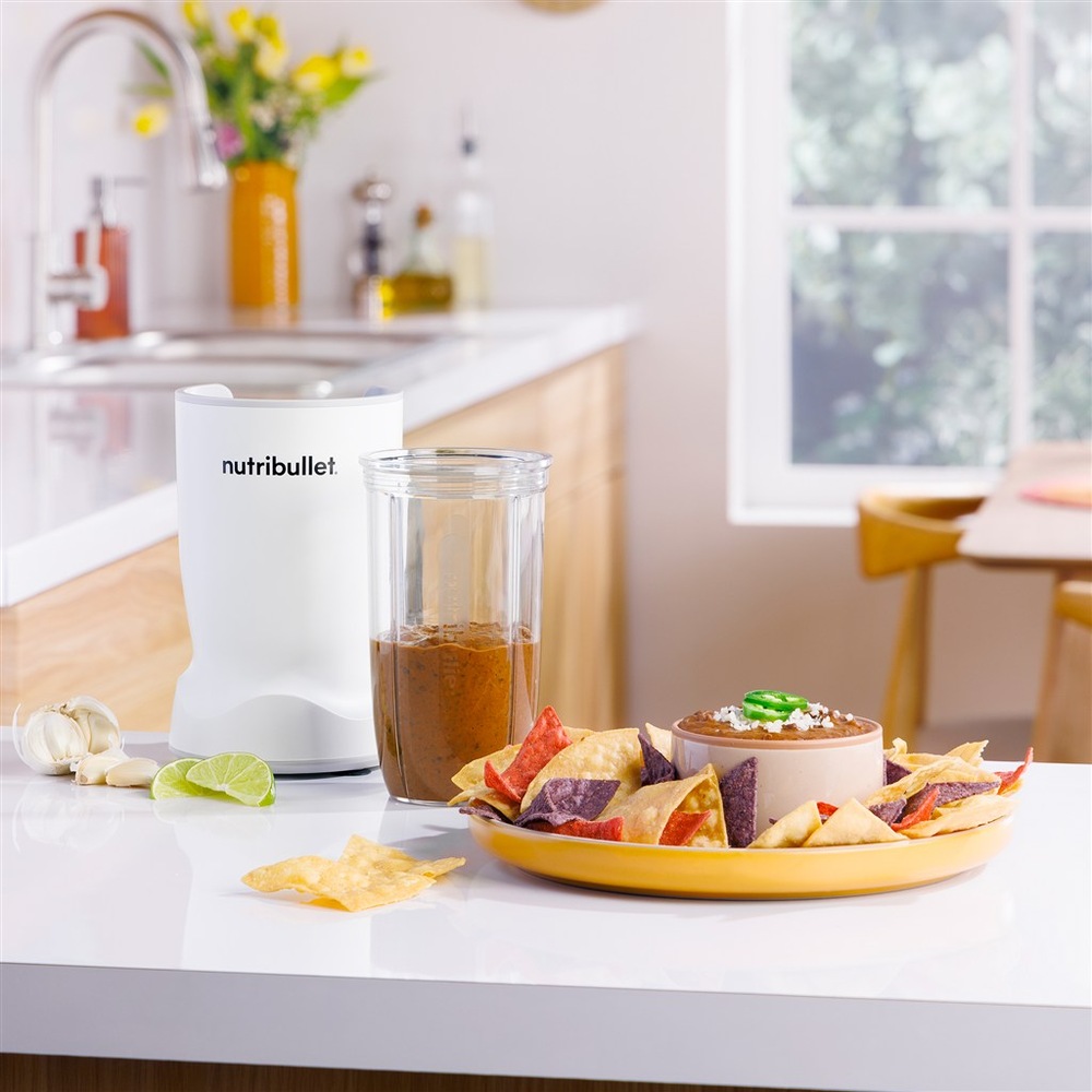 Mixér NutriBullet použitý k přípravě omáčky, vedle talíře s tortilla chips a dipem.