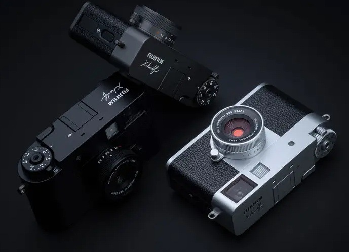 Digitální fotoaparát Fujifilm X half černý/šedý Fotoaparáty Fujifilm X half v černém a stříbrném provedení s kompaktním retro designem položené na tmavém podkladu
